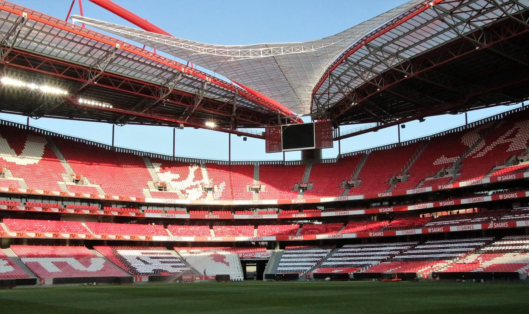 Tomt Estádio da Luz i Lisboa med røde tribuner, grønn gressmatte og det buede taket over arenaen