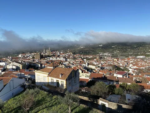 Utsikt over hustakene i Portalegre med katedraltårnene og grønne åser under et teppe av morgentåke