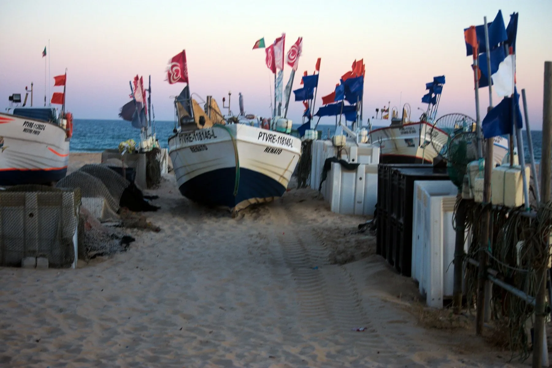 Fiskebåter med flagg trukket opp på sandstranden i Monte Gordo i solnedgang