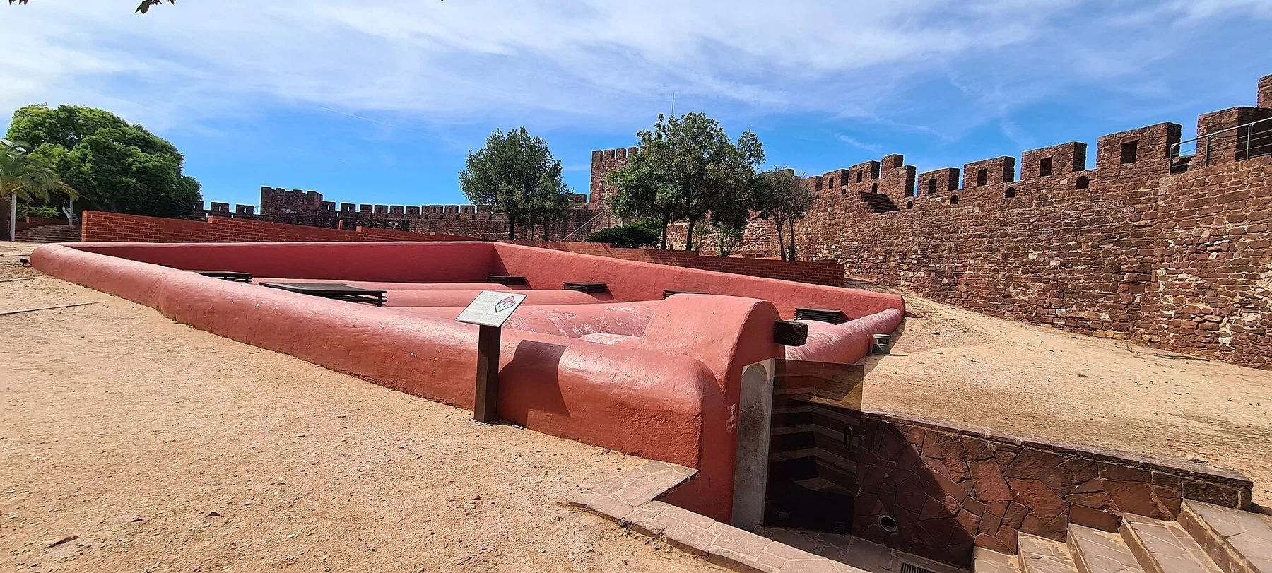 De røde sandsteinsmurene og cisternen inne i maurerborgen i Silves under blå himmel