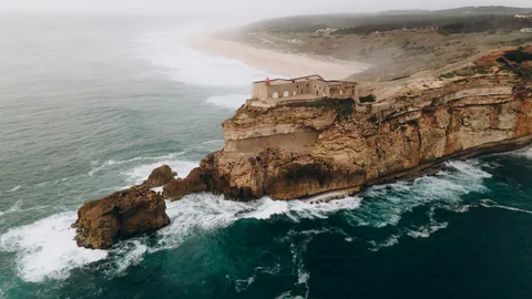 Dronebilde av klippen ved Nazare med fyret og bølgene under