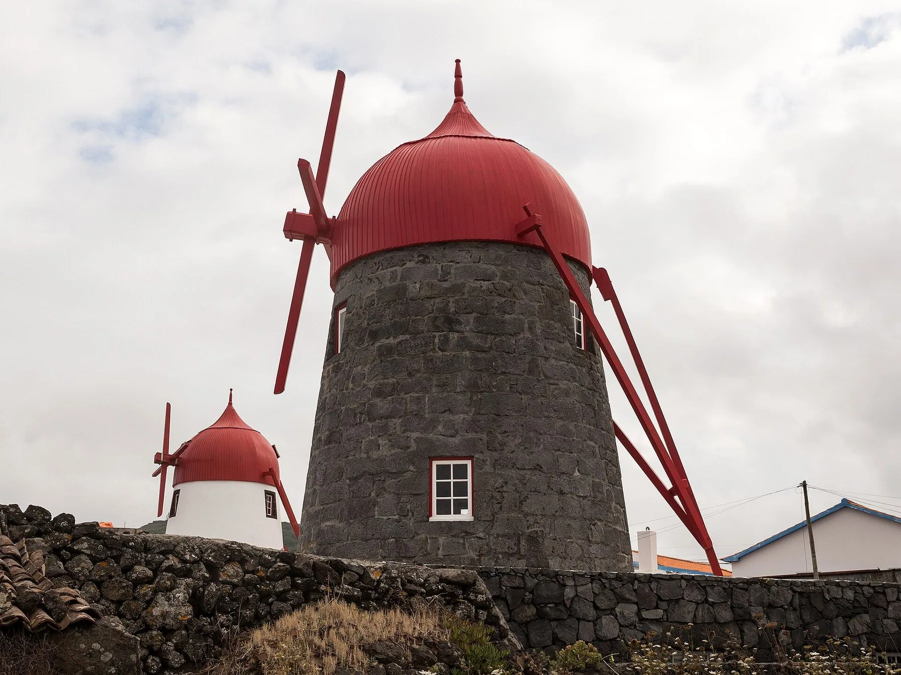 Tradisjonell vindmølle av mørk lavastein med rødt tak og røde vinger bak en steinmur på Graciosa