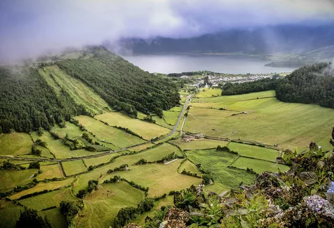 Lave skyer og tåke over kraterdalen ved Sete Cidades, med grønne åkerlapper og innsjøen i bakgrunnen