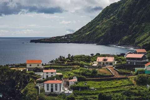 Liten landsby på en fajã under bratte, grønne klipper ved havet på São Jorge