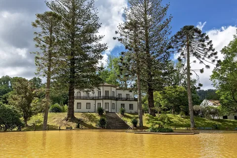 Det okergule varmtvannsbassenget i Parque Terra Nostra i Furnas, med høye araukarier og det hvite herskapshuset bak