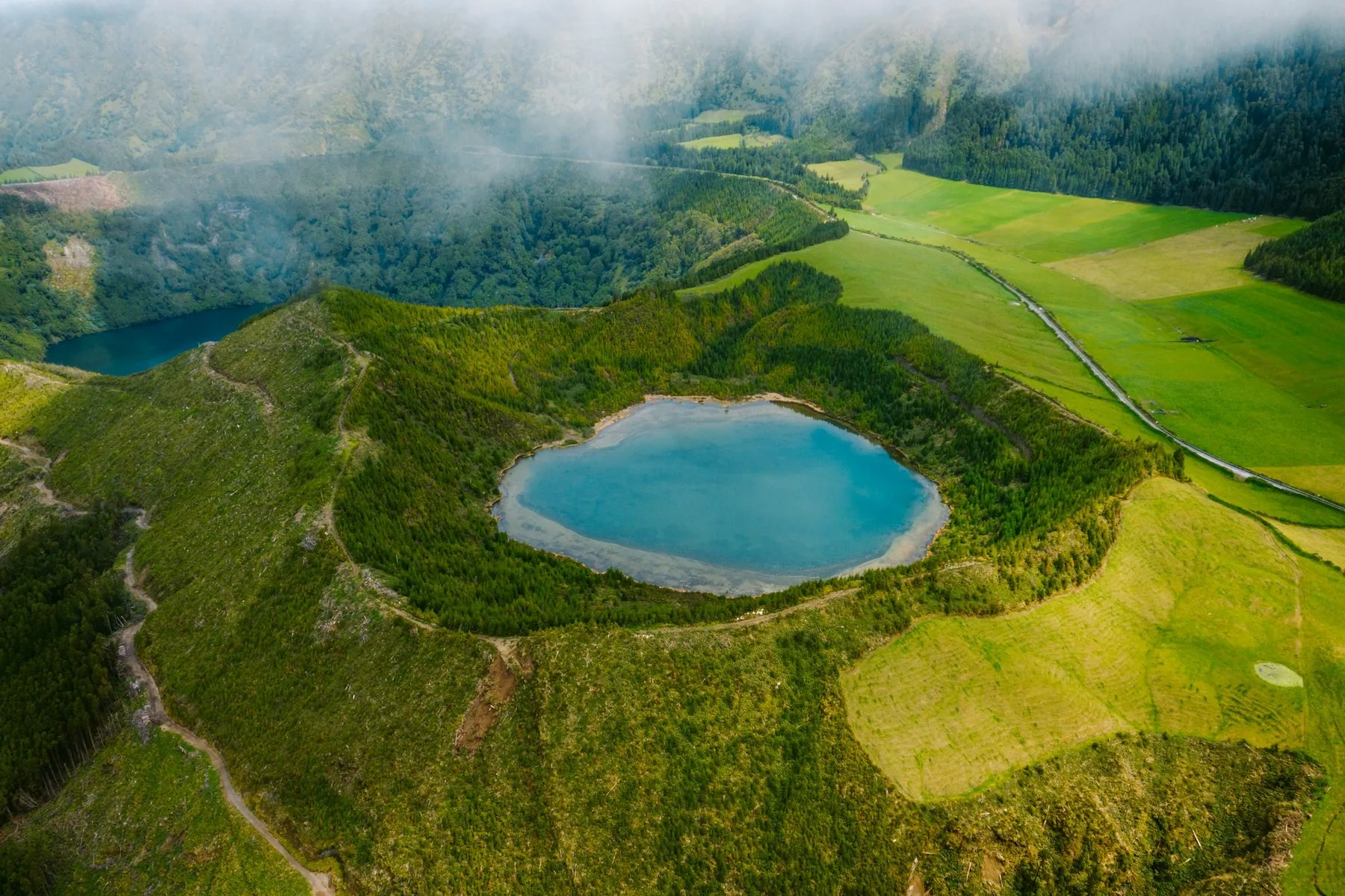 Luftfoto av en kratersjø omgitt av grønn skog på Azorene