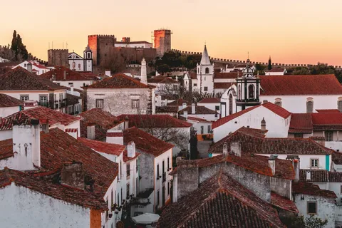 Hvite hus med røde tegltak i gyllent solnedgangslys i landsbyen Obidos