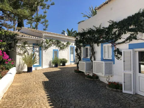 Hvitkalkede hus med blå kanter, klatreplanter og brostein i solskinn i Vila Verde i Algarve