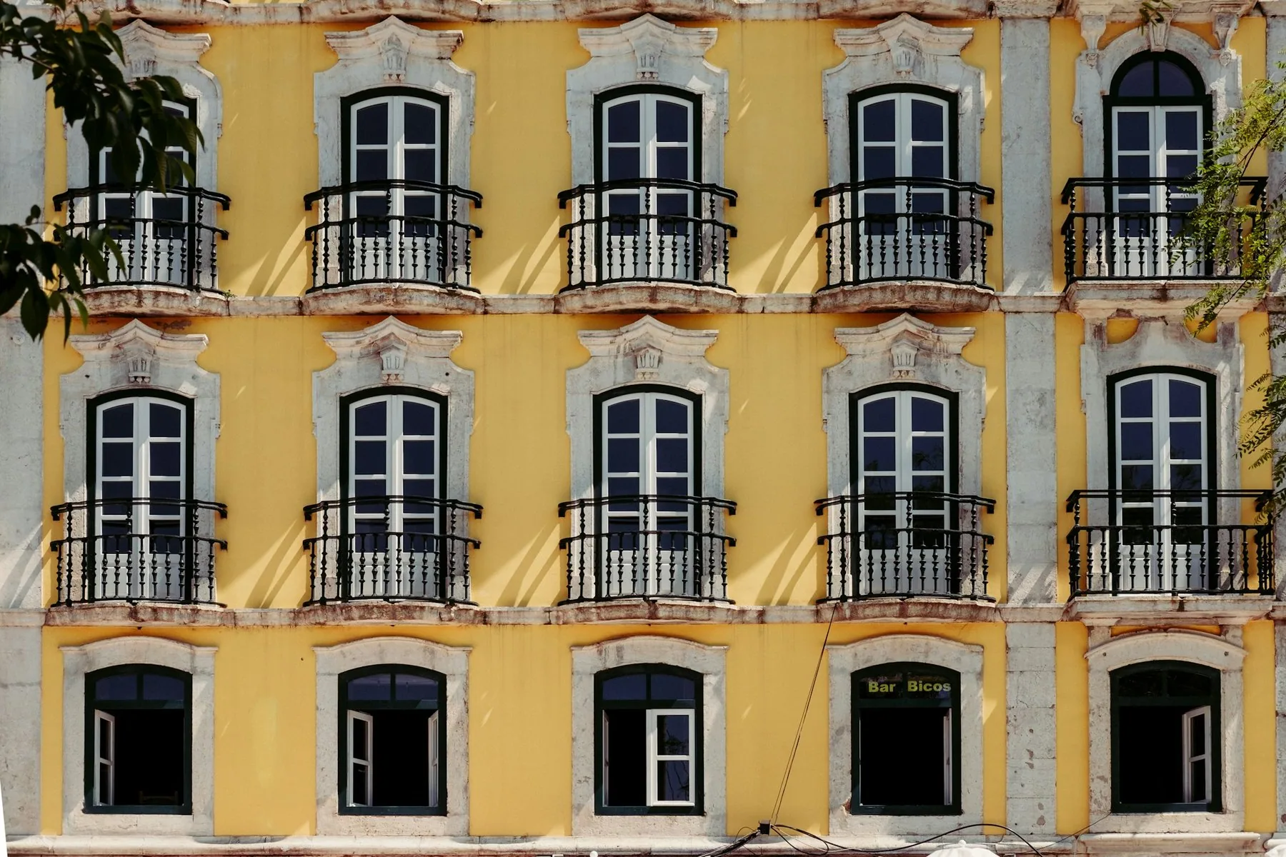 Gul bygårdsfasade med rekker av vinduer, smijernsbalkonger og hvite dekorlister i Alfama i Lisboa