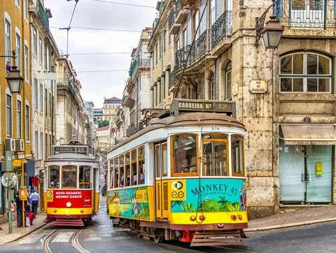 Gul og hvit trikk på skinnene i en gate med gamle bygårder i Lisboa