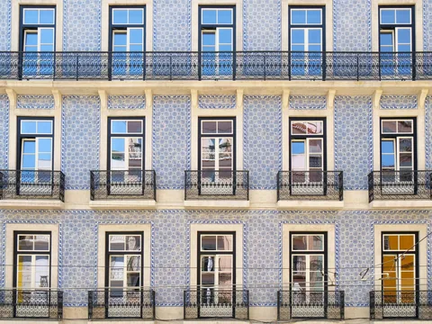 Rader av vinduer med smijernsbalkonger på en bygård med blå og hvite fliser i Lisboa
