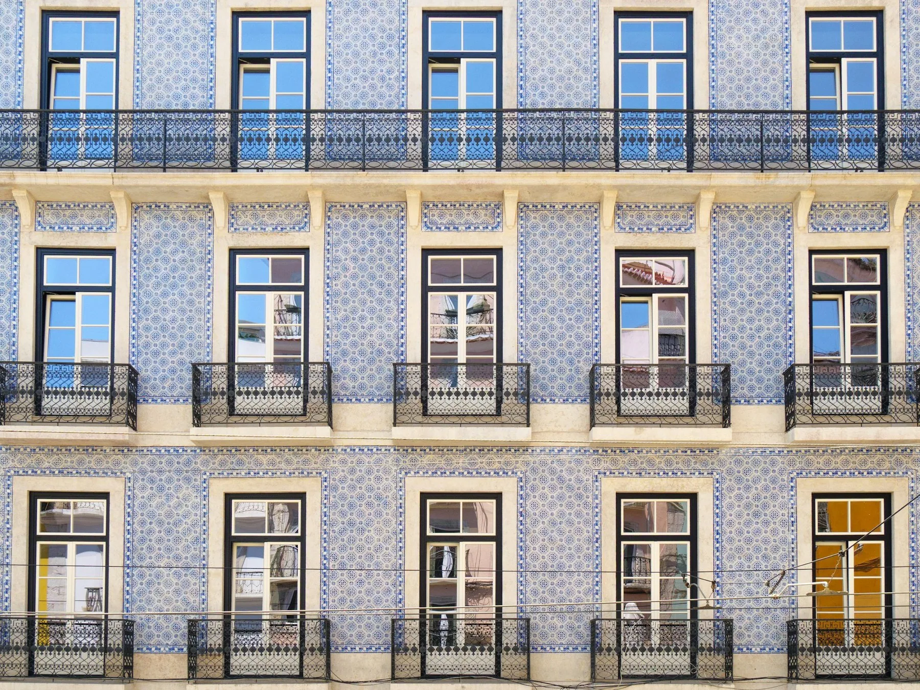 Rader av vinduer med smijernsbalkonger på en bygård med blå og hvite fliser i Lisboa