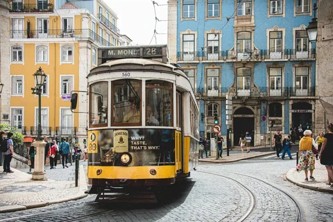 Gul og hvit trikk foran en hvit bygård i en solfylt gate i Lisboa