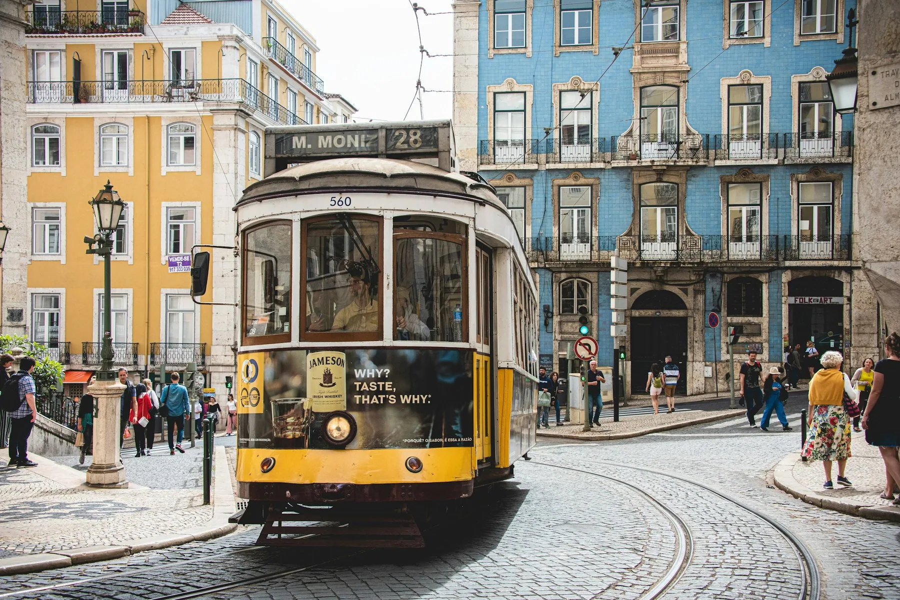 Gul og hvit trikk foran en hvit bygård i en solfylt gate i Lisboa