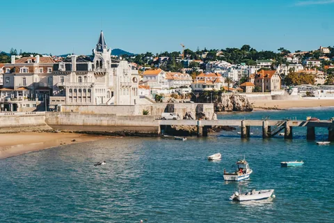 Hvit og blå fiskebåt på rolig sjø foran hvite bygninger i Cascais
