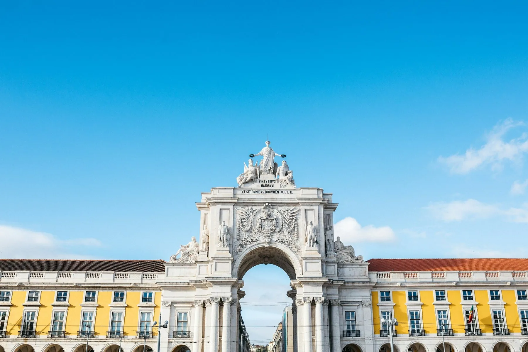 De gule buegangene rundt Praca do Comercio i Lisboa under blå himmel