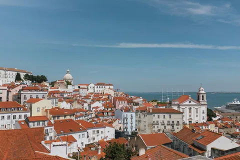 Utsikt over Alfamas røde tak og kirketårn mot Tejo-elven under en klar blå himmel i Lisboa