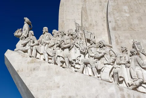 Steinfigurene av sjøfarere på Padrão dos Descobrimentos i Belém mot en dypblå himmel