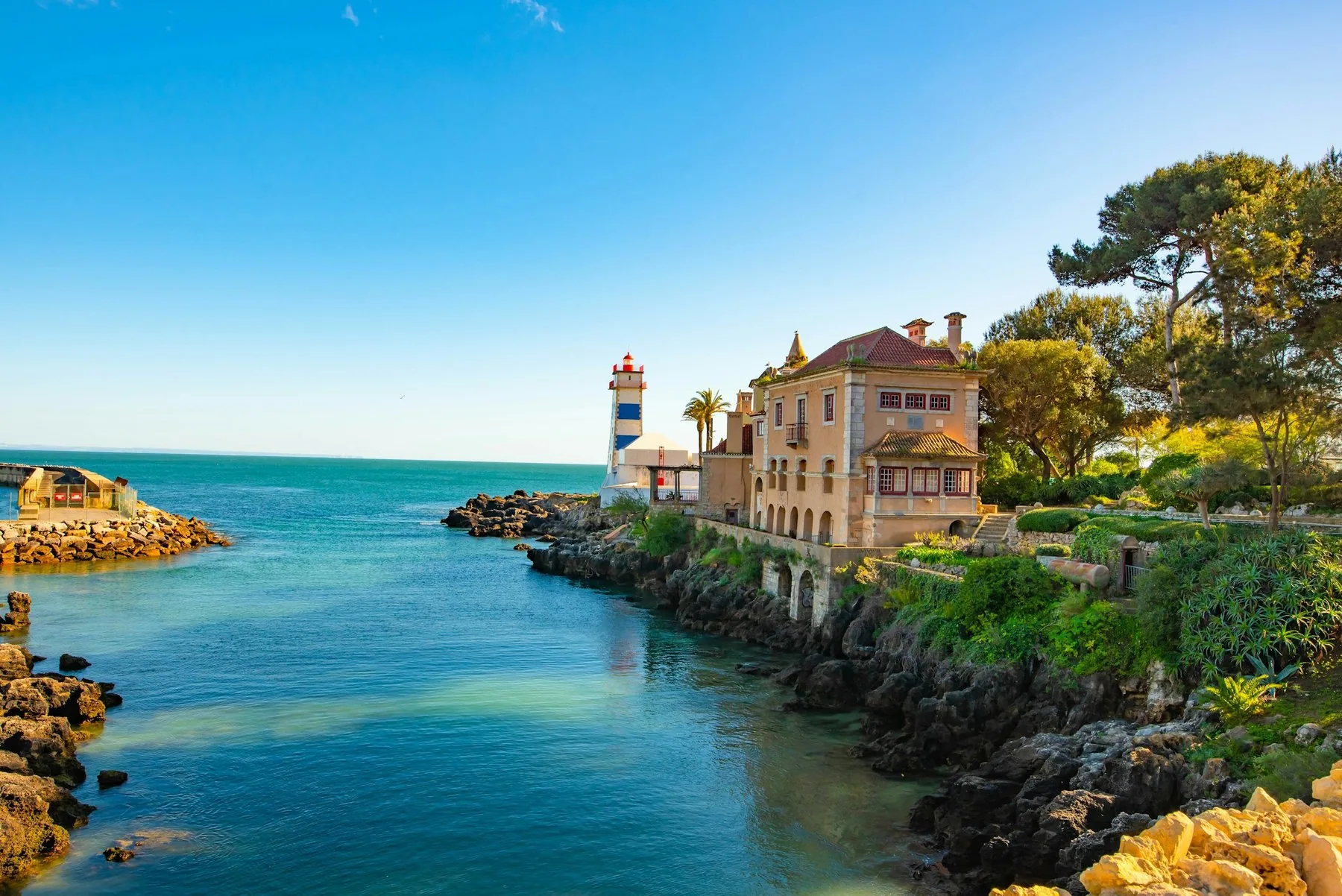 Hvit villa med brun stein ved vannkanten i Cascais under blå himmel