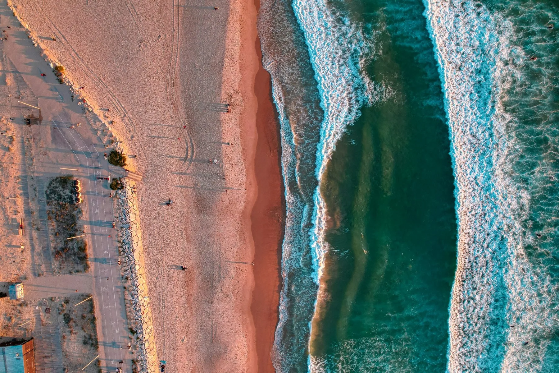 Den lange sandstranden i Costa da Caparica sett fra luften med bølger som ruller inn