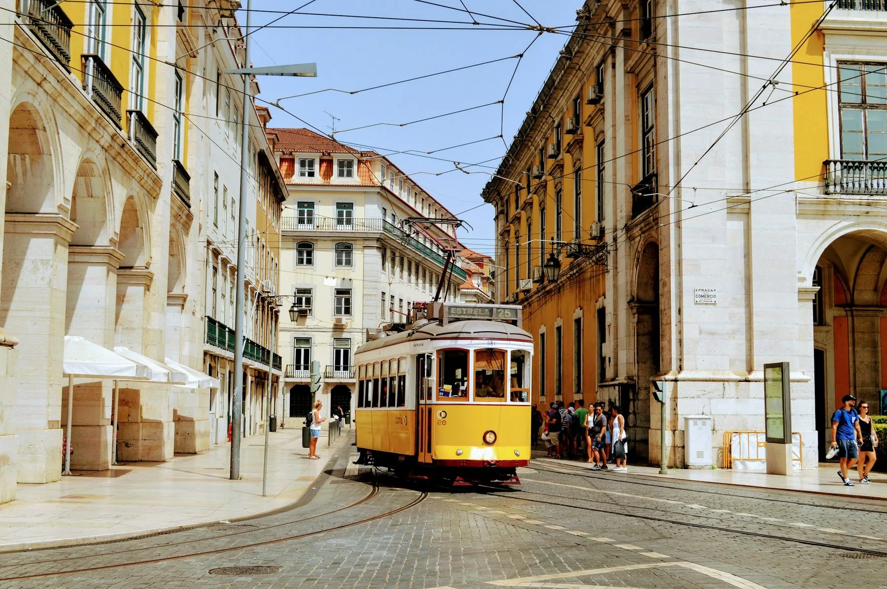 Gul trikk på vei gjennom en smal gate med gamle bygårder i Lisboa