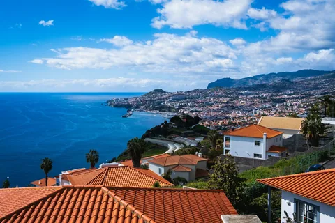 Hvite og brune hus tett i tett langs Funchal-bukta med havet like ved
