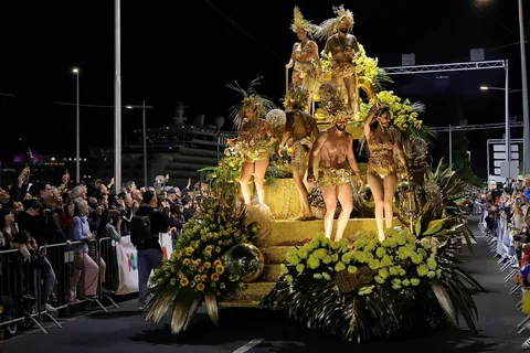 Opplyst gullfarget paradevogn med blomsterdekor og dansere under karnevalsparaden i Funchal om kvelden, med publikum langs gata
