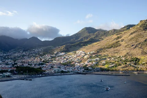 Machico-bukta i kveldssol, med byen langs strandpromenaden og tørre fjellsider over bebyggelsen