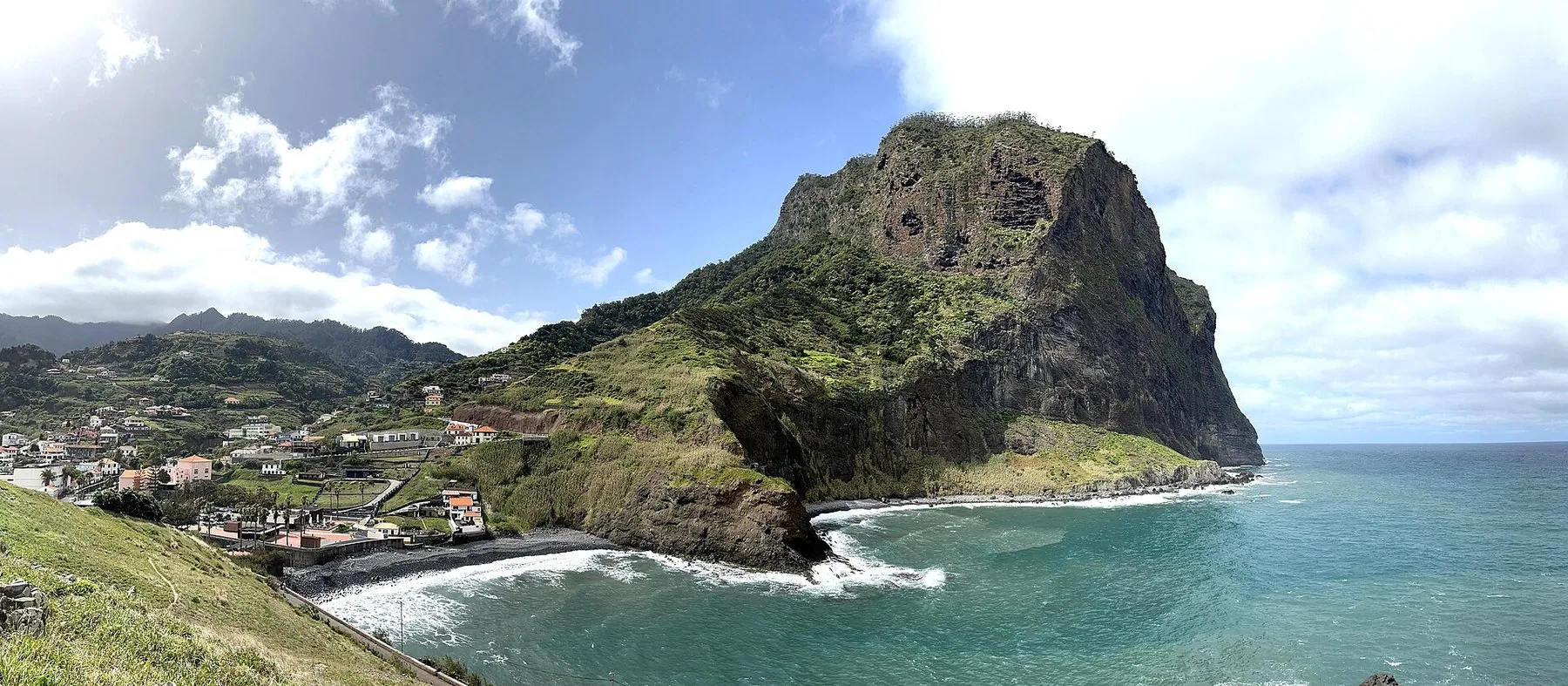 Klippen Penha d'Águia rager over bukta og husene i Porto da Cruz med turkist hav og brenninger