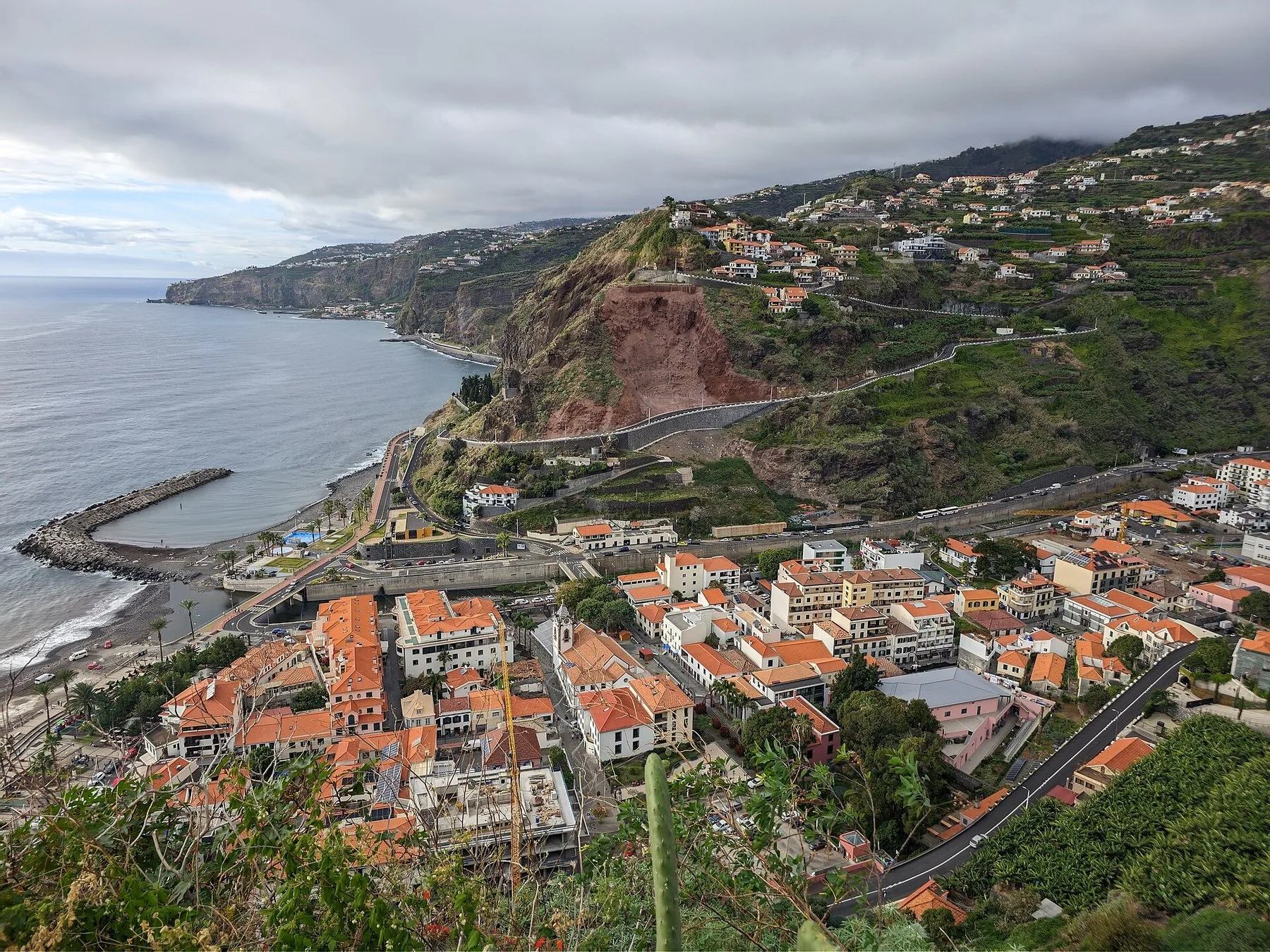 Ribeira Brava sett fra utsiktspunkt: rødtakte hus i dalbunnen, molo ved havet og bratte terrasserte fjellsider