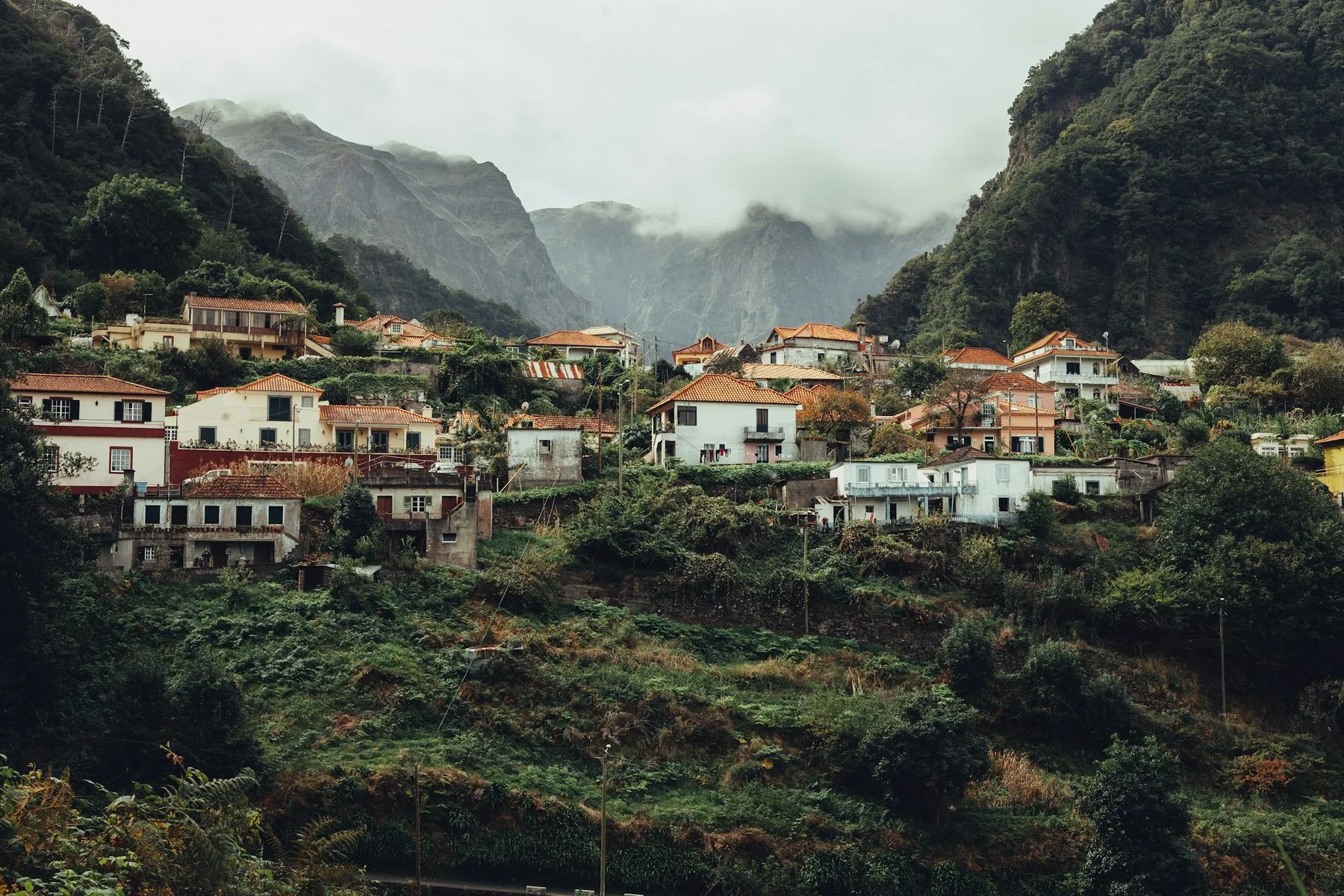 Hus spredt oppover de grønne fjellsidene på Madeira med skyer over toppene