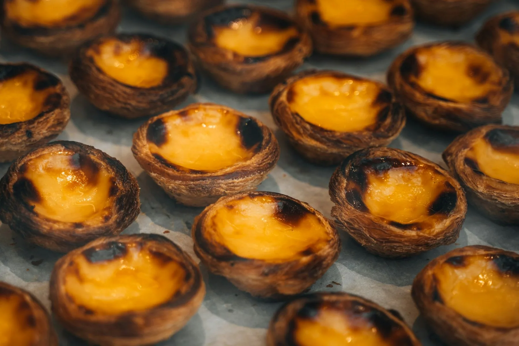 Rader med gyllenbrune portugisiske eggeterter, pastéis de nata, rett fra ovnen