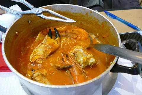 Gryte med arroz de marisco med krabbeklør og reker på et restaurantbord i Lisboa, med skalldyrtang på kanten