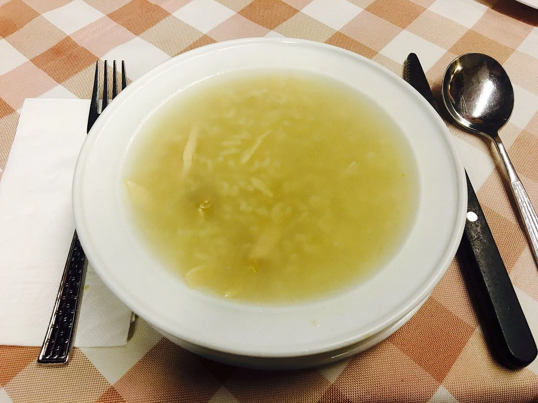 Tallerken med canja de galinha, portugisisk kyllingsuppe med ris, på en rutete duk med skje og bestikk