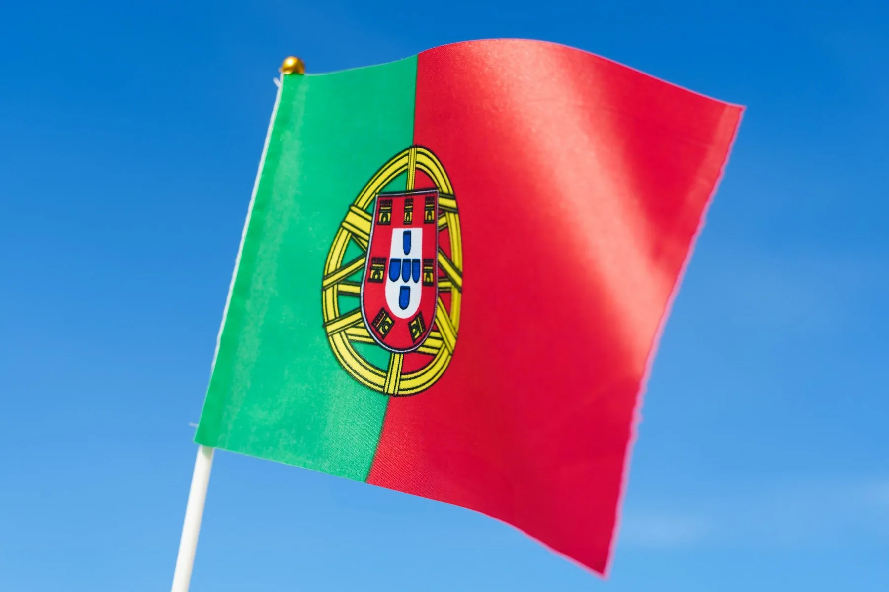 Det røde og grønne portugisiske flagget vaier i vinden mot en lys himmel