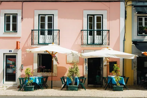 To hvite parasoller over uteserveringen foran en rosa og hvit husfasade i Lisboa