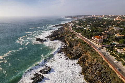 Kystveien langs klippene ved Boca do Inferno i Cascais med villaer, bølger og Estoril i det fjerne