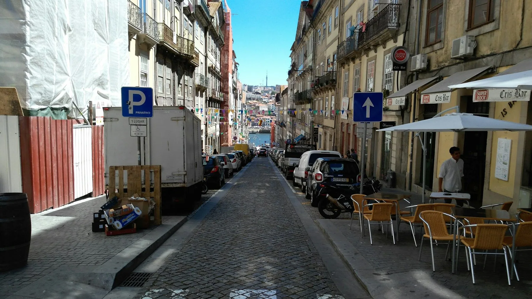 Smal gate i Porto med kafeebord langs fortauet og parkerte biler
