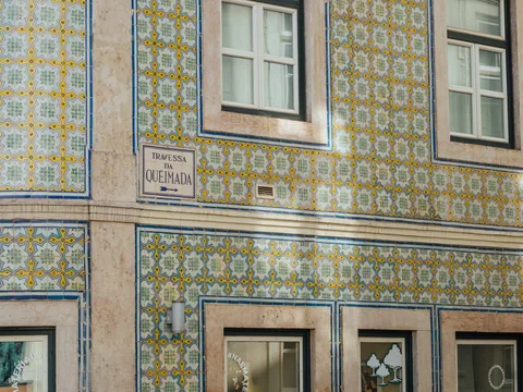 Bygård i Lisboa kledd med gule og blå azulejofliser, med hvite vinduer og gateskiltet Travessa da Queimada