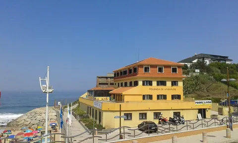 Det gule vandrerhjemmet Pousada de Juventude ved stranden Praia da Areia Branca, med havet og strandpromenaden til venstre
