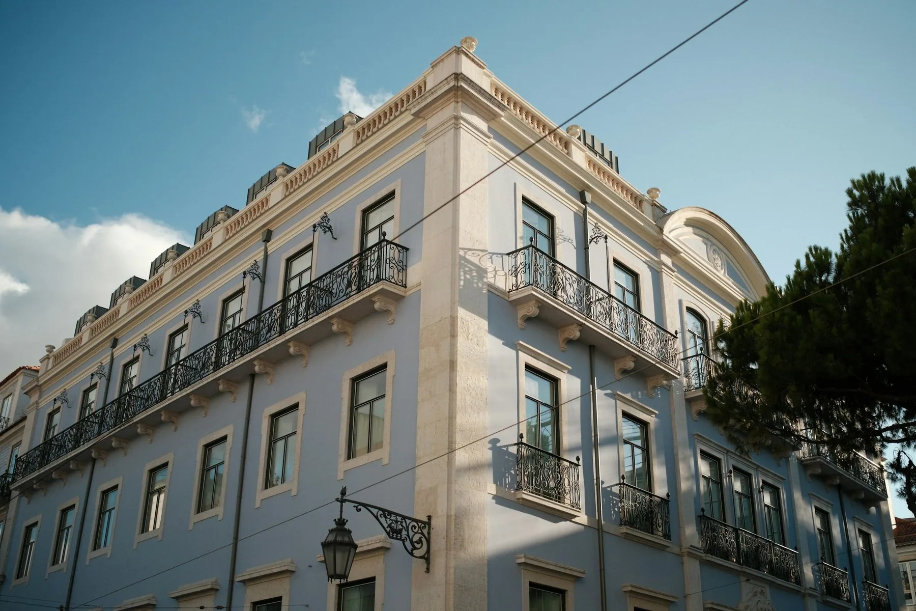 Lyseblå bygård med smijernsbalkonger i Rua do Alecrim i Lisboa under klar himmel