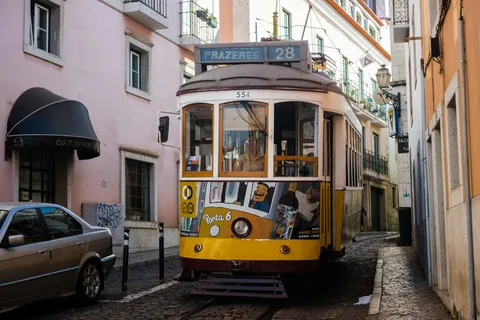 Gul og blå trikk kjører gjennom en smal gate i Lisboa med parkerte biler langs fortauet