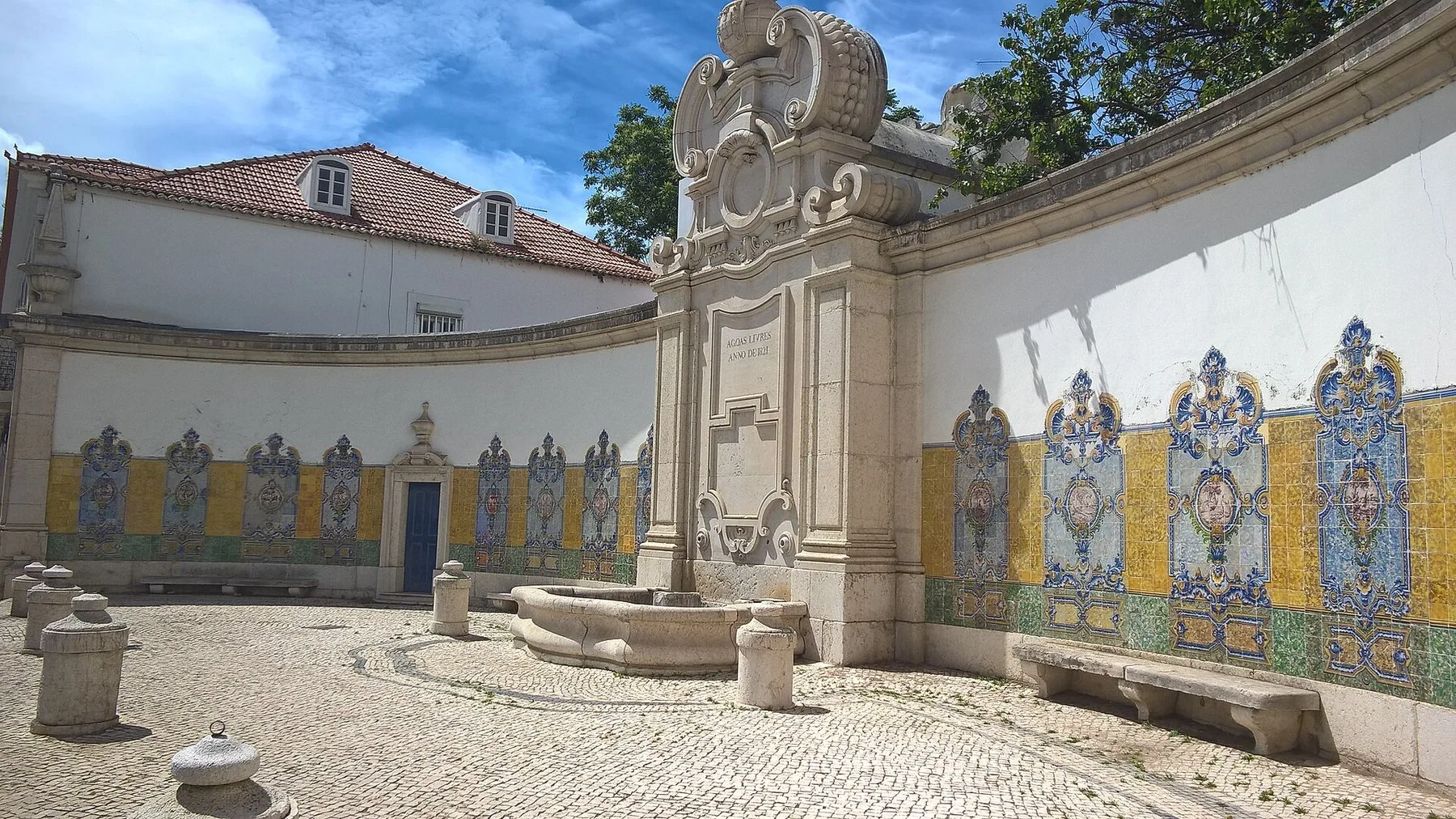 Den historiske fontenen Chafariz da Junqueira i Lisboa med azulejo-fliser langs den buede muren