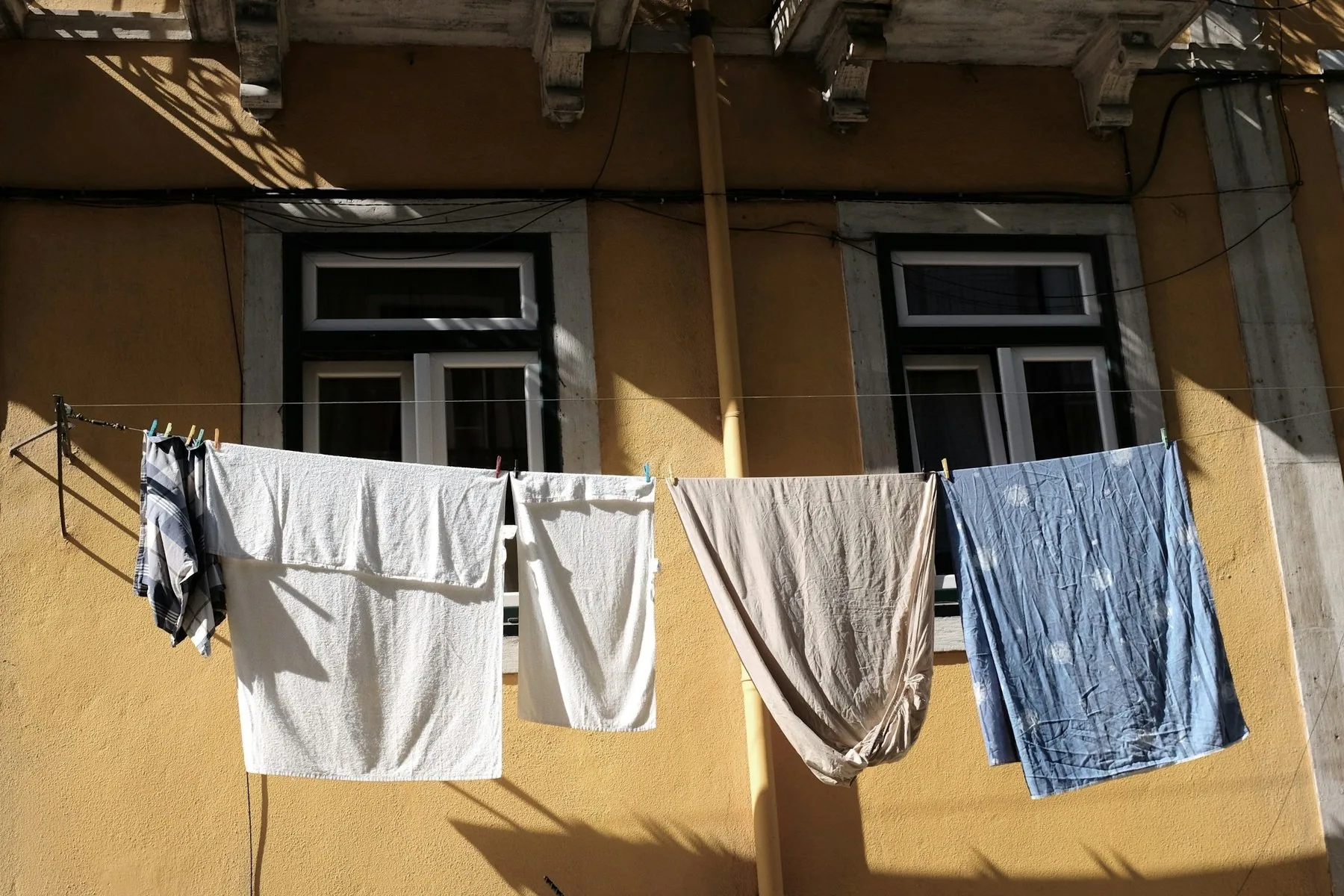 Håndklær og klær henger til tørk på en snor foran vinduene på en okergul husfasade i Lisboa