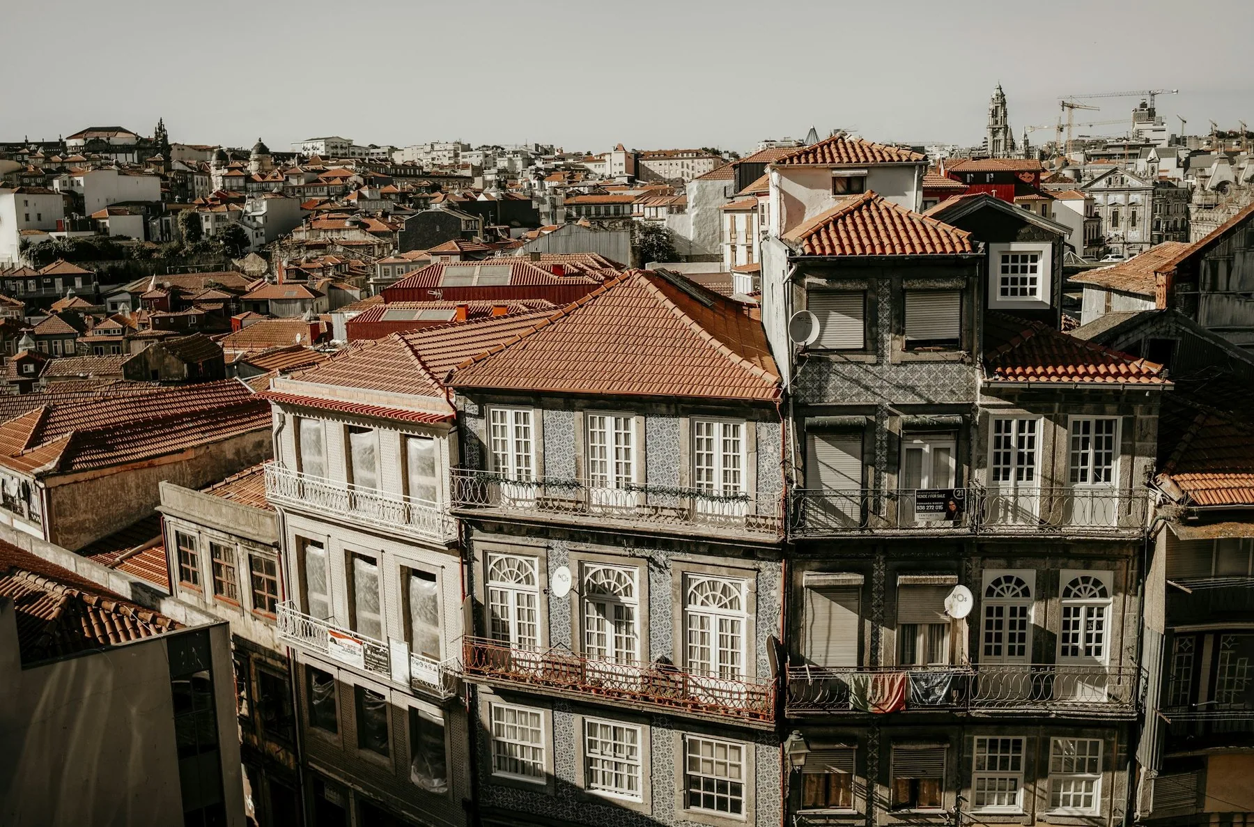Tette rekker av gamle bygårder med flisfasader og brune teglsteinstak under disig himmel i Porto