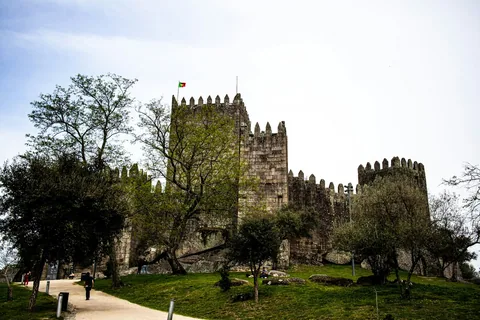 Middelalderborgen i Guimarães med steintårn bak grønne trær og gressplen