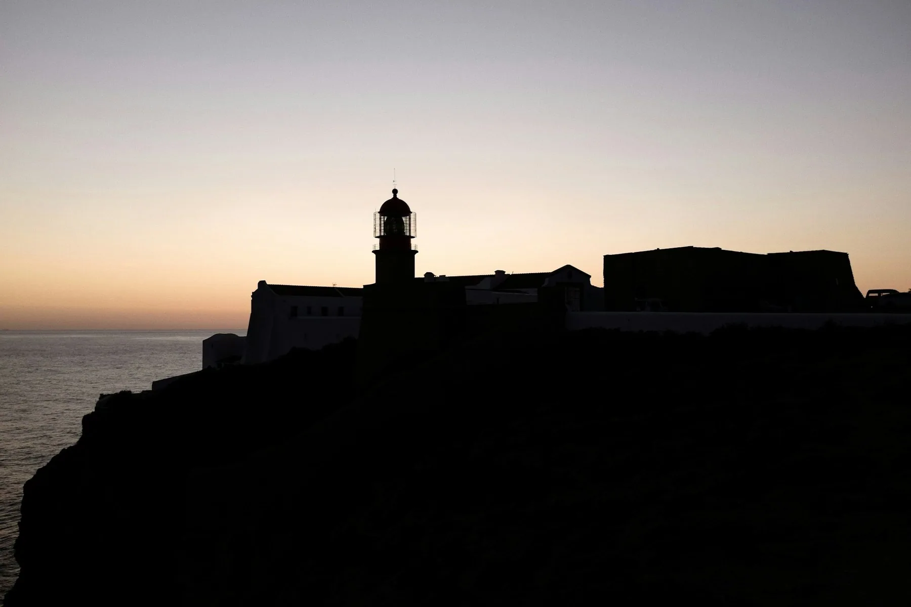 Fyrtårn og festningsmur i silhuett på en klippe over Atlanterhavet ved Sagres