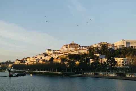 Coimbra sett over Mondego-elva i kveldslys, med universitetet øverst på åsen