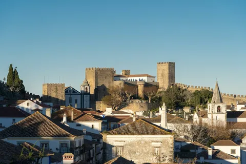 Borgen og bymuren i Obidos over teglrode tak og hvitkalkede hus i lavt ettermiddagslys