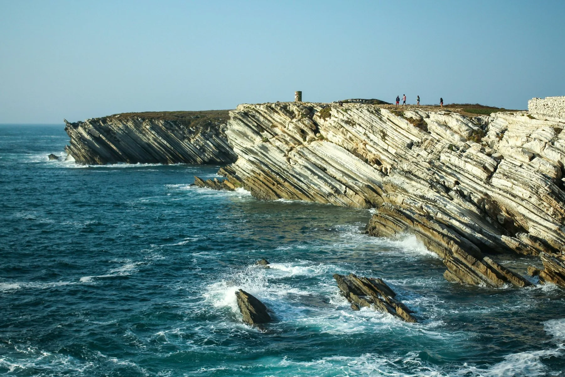 Skråstilte kalksteinsklipper på Baleal-neset ved Peniche med Atlanterhavet som bryter mot fjellet